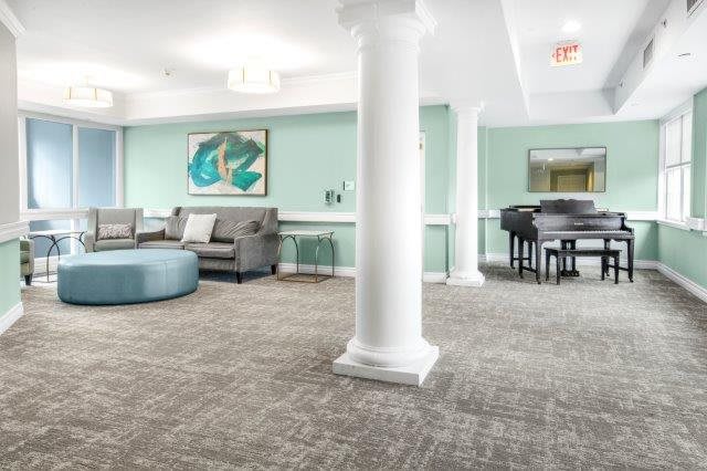 A modern lounge area with comfortable seating, a piano, and artwork on the walls.