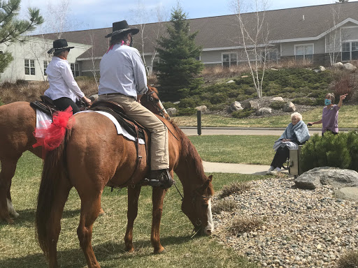 Two riders on horseback enjoy a sunny day in the park while another person watches.