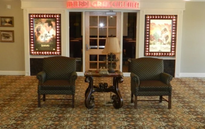 A cozy seating area in a movie theater lobby, featuring two armchairs and a table with a lamp, flanked by movie posters.