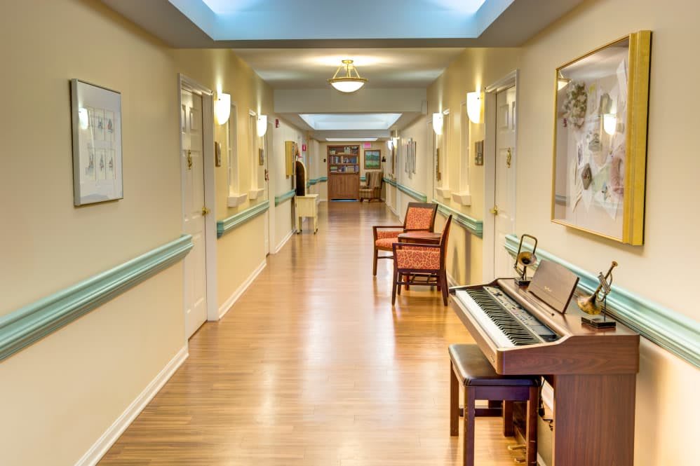 A long hallway with a piano and chairs lining the walls, leading to a distant entrance.