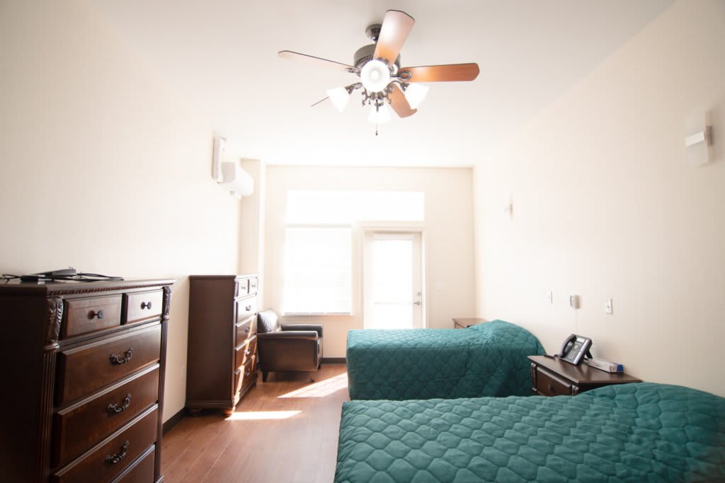 A bright bedroom with two beds, a ceiling fan, and ample natural light.