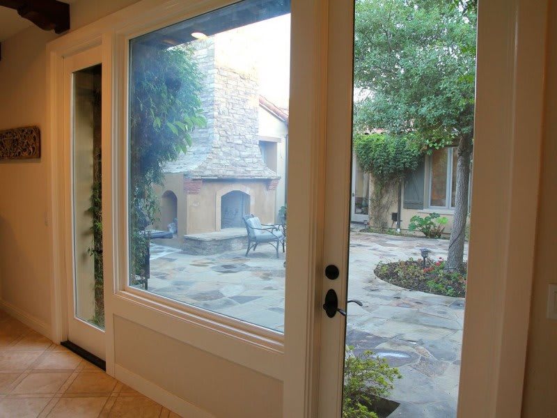 View of a charming courtyard with outdoor seating and stone flooring through a large window.