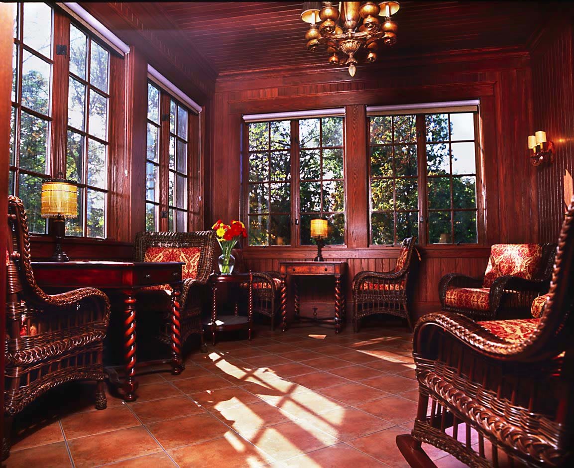 A cozy sunroom filled with natural light, featuring wooden furniture and large windows.