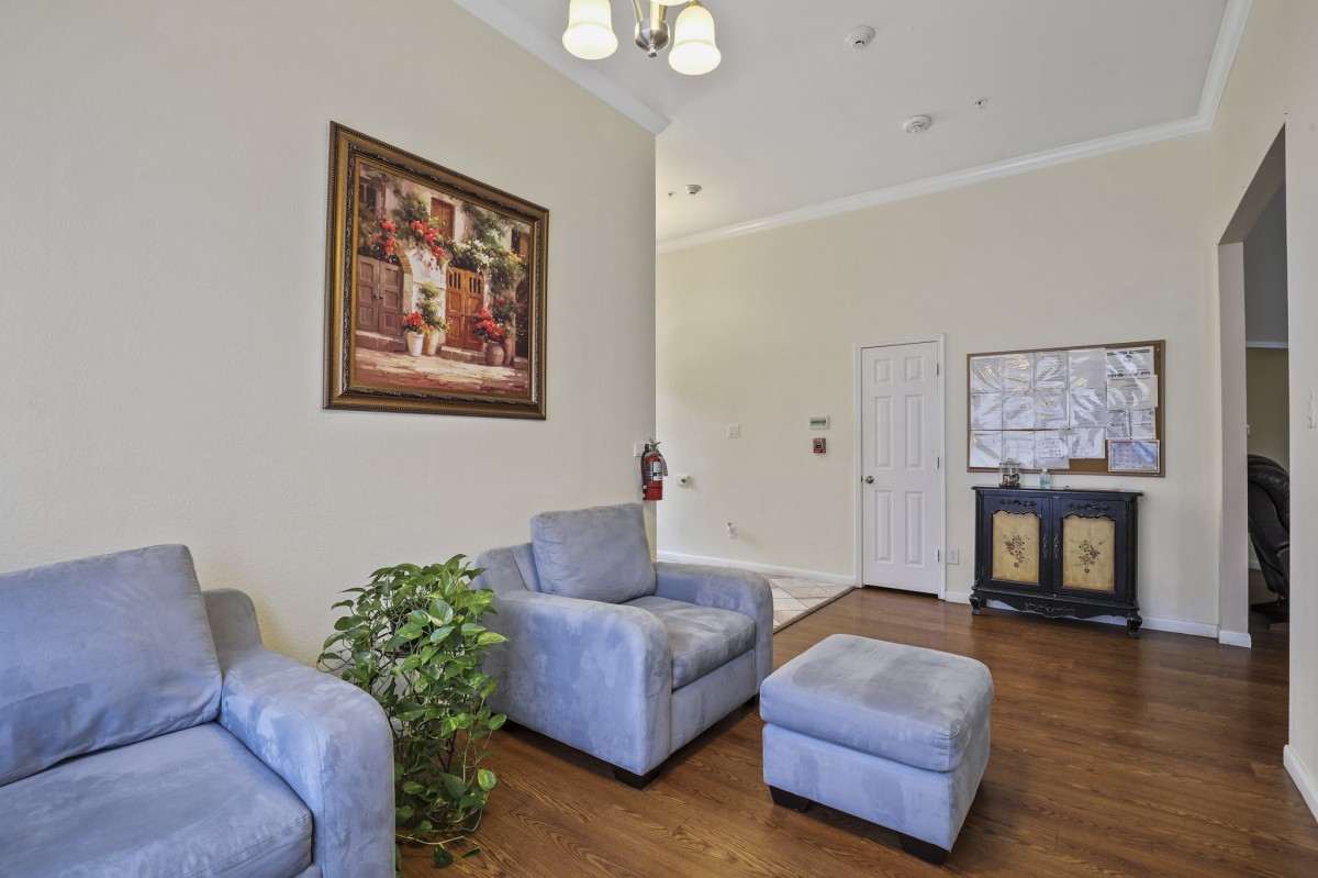 A cozy living room with armchairs, an ottoman, artwork on the wall, and a potted plant.