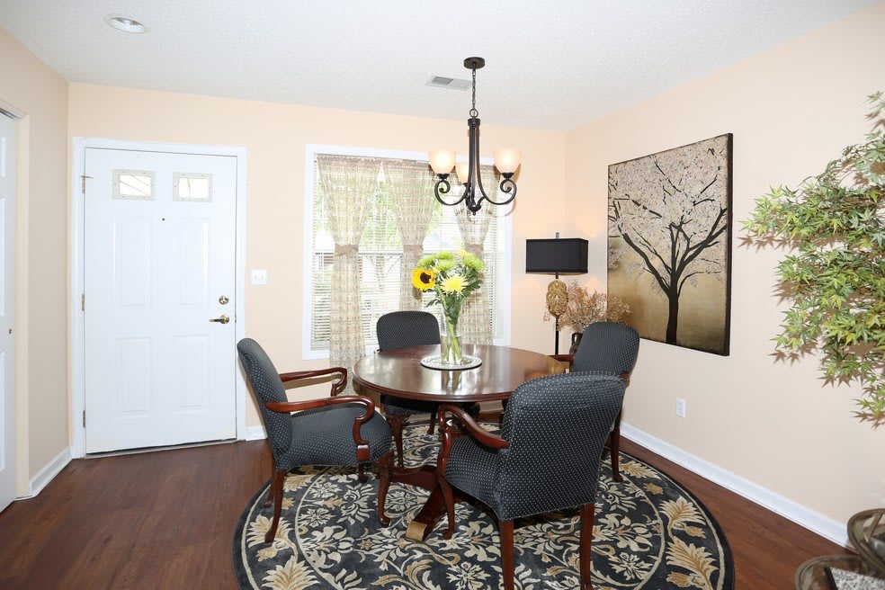 A cozy dining room with a round table, surrounded by chairs and decorated with sunflowers in a vase, under a stylish chandelier.