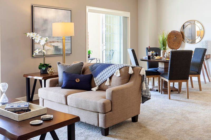 A cozy living room with a beige sofa and blue pillows, connected to a dining area.