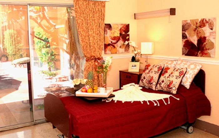 A cozy bedroom with red bedding and elegant decor, featuring a lamp and indoor plants.