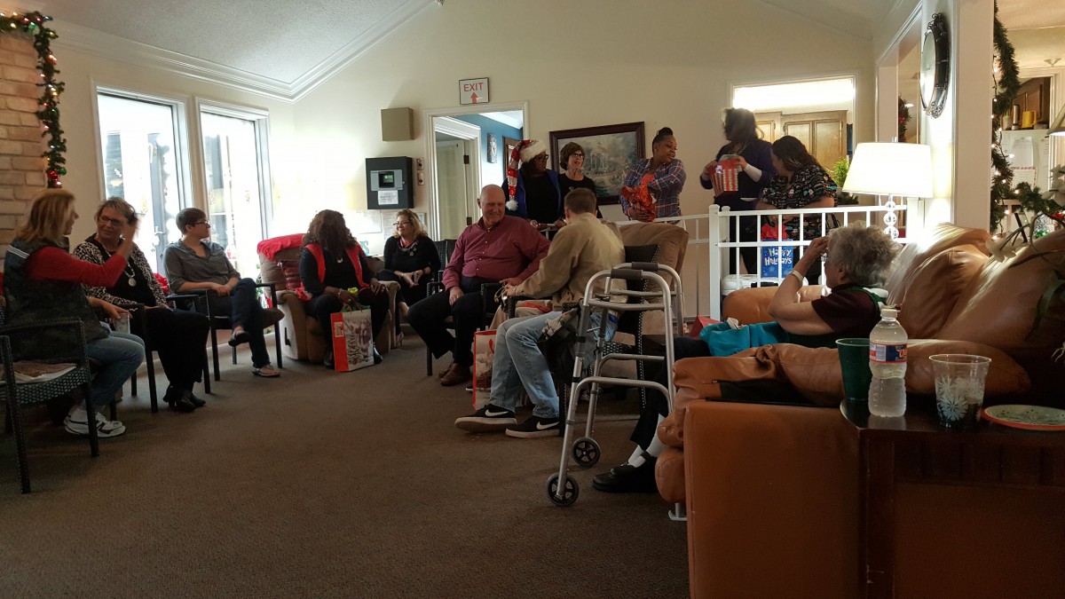 A community gathering with people seated indoors, some using walkers.