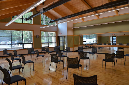 A spacious activity room with chairs arranged for gathering, featuring large windows that allow natural light to illuminate the wooden floor.