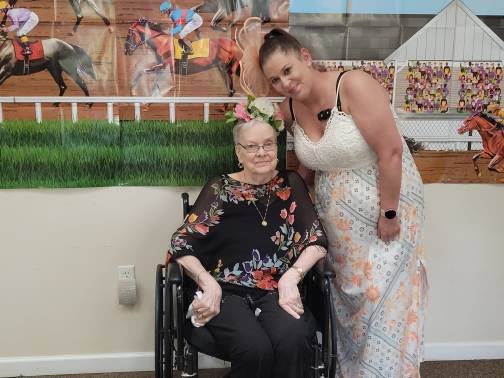 Two women celebrating indoors, one seated in a wheelchair and wearing floral clothing.