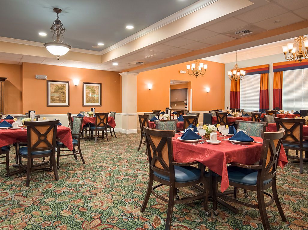 A well-decorated dining room with several tables and chairs, featuring orange walls and a patterned carpet.