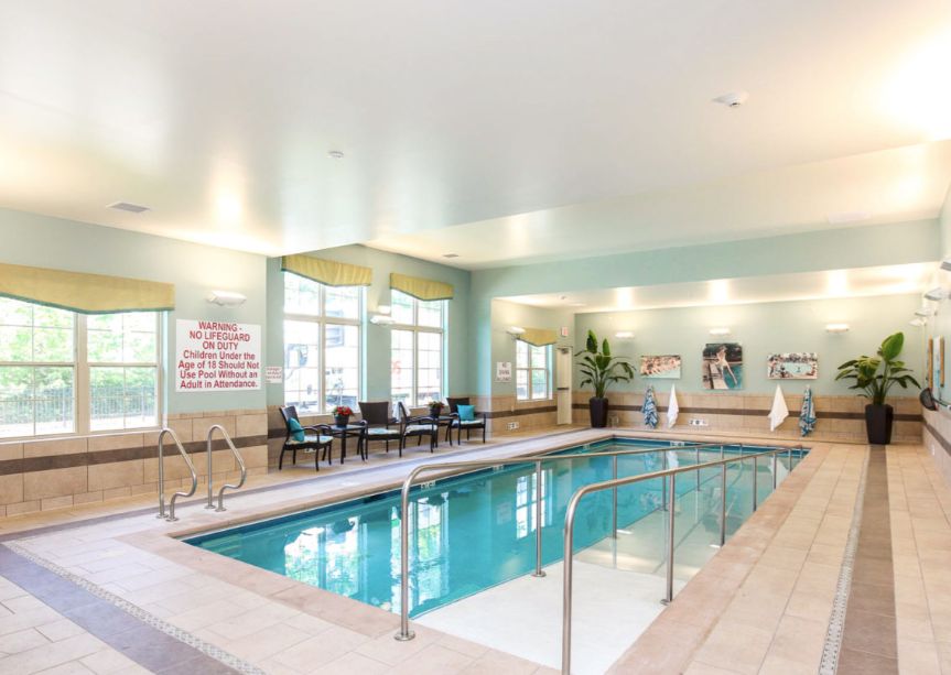 A well-lit indoor swimming pool area with seating along the side.