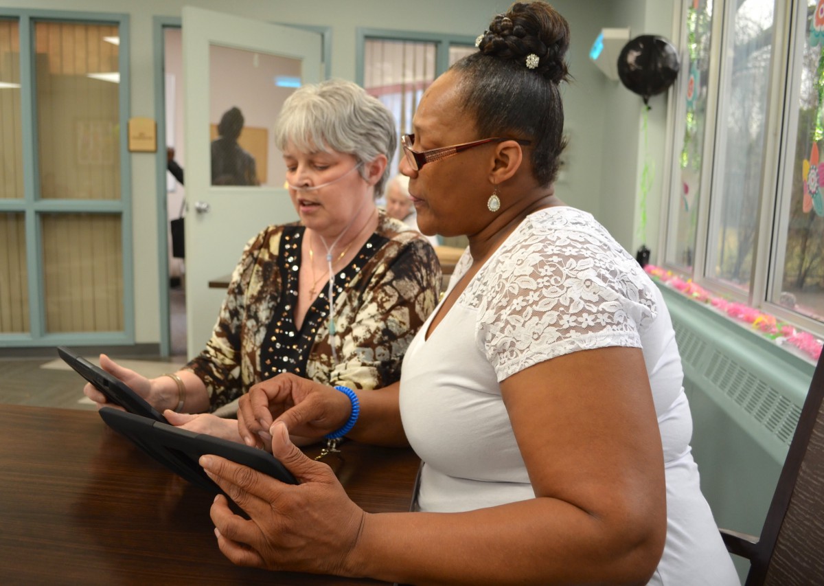Two women collaborating and discussing information on a tablet in an office setting.