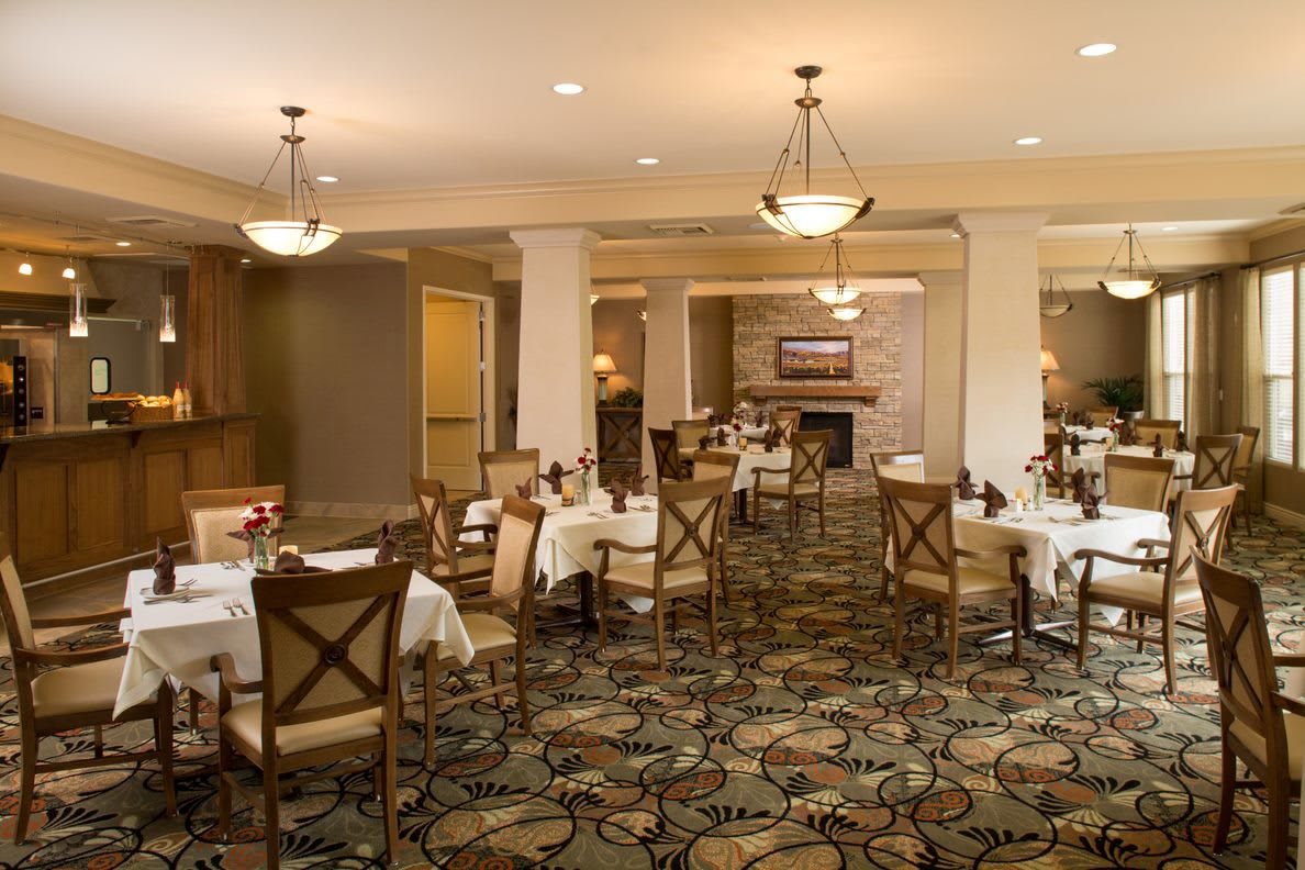 An elegant dining area with neatly arranged tables and chairs, illuminated by chandeliers.