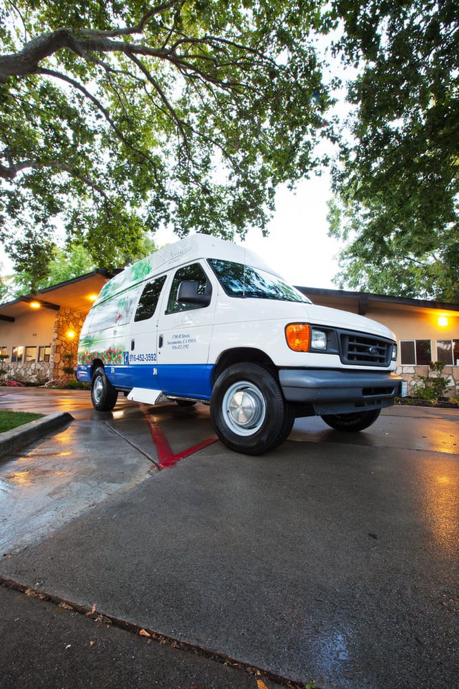 A white and blue van parked in a lot next to a building, surrounded by trees.