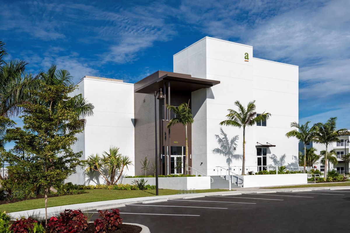 A modern commercial building with a sleek design, surrounded by palm trees under a clear blue sky.