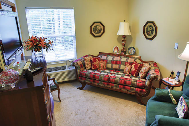 A cozy living room with a patterned sofa, decorative pillows, and a standing lamp by the window.