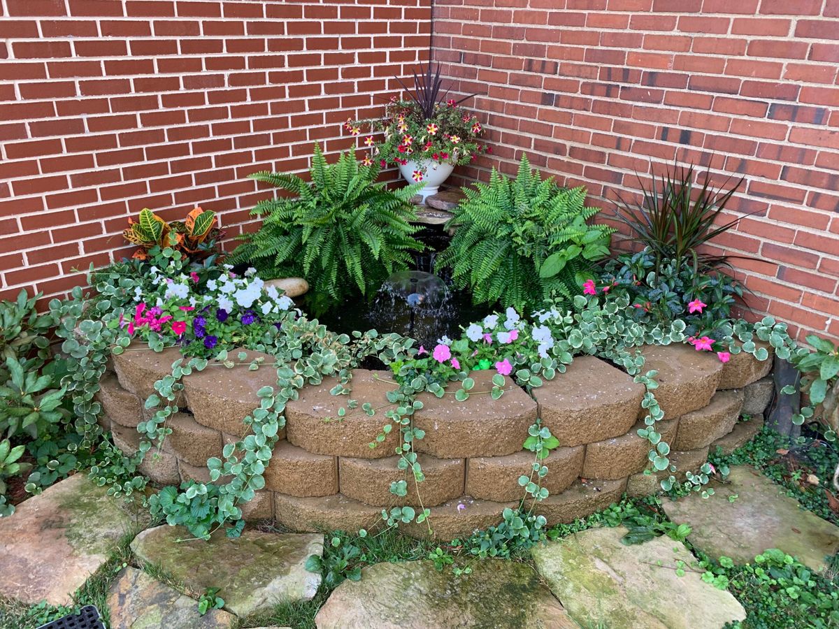 A small garden with colorful flowers and lush plants against a brick wall.