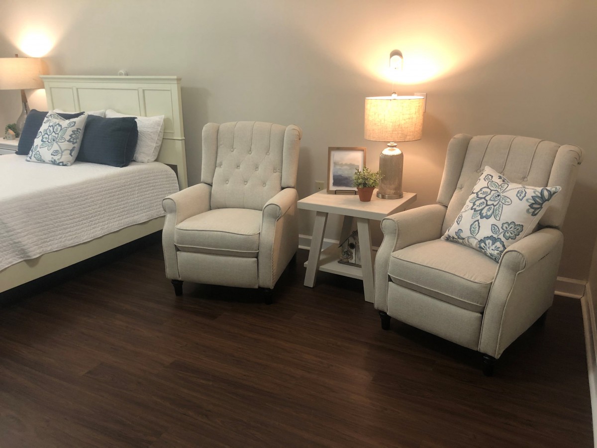 A cozy bedroom with two armchairs, a side table, and a lamp next to the bed.