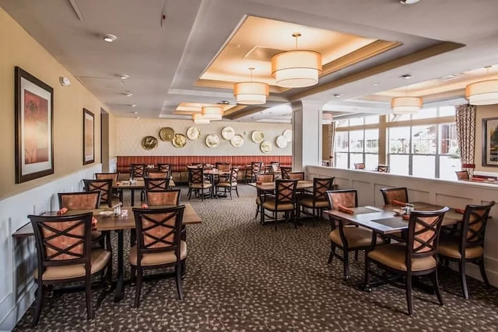 An empty restaurant dining area with neatly arranged tables and chairs, elegantly decorated with warm lighting and wall accents.
