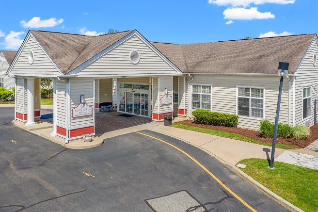 The image shows the entrance of a building with a driveway and parking area.