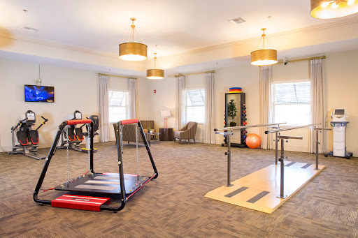 A well-lit rehabilitation and fitness space featuring exercise equipment such as a treadmill and parallel bars.