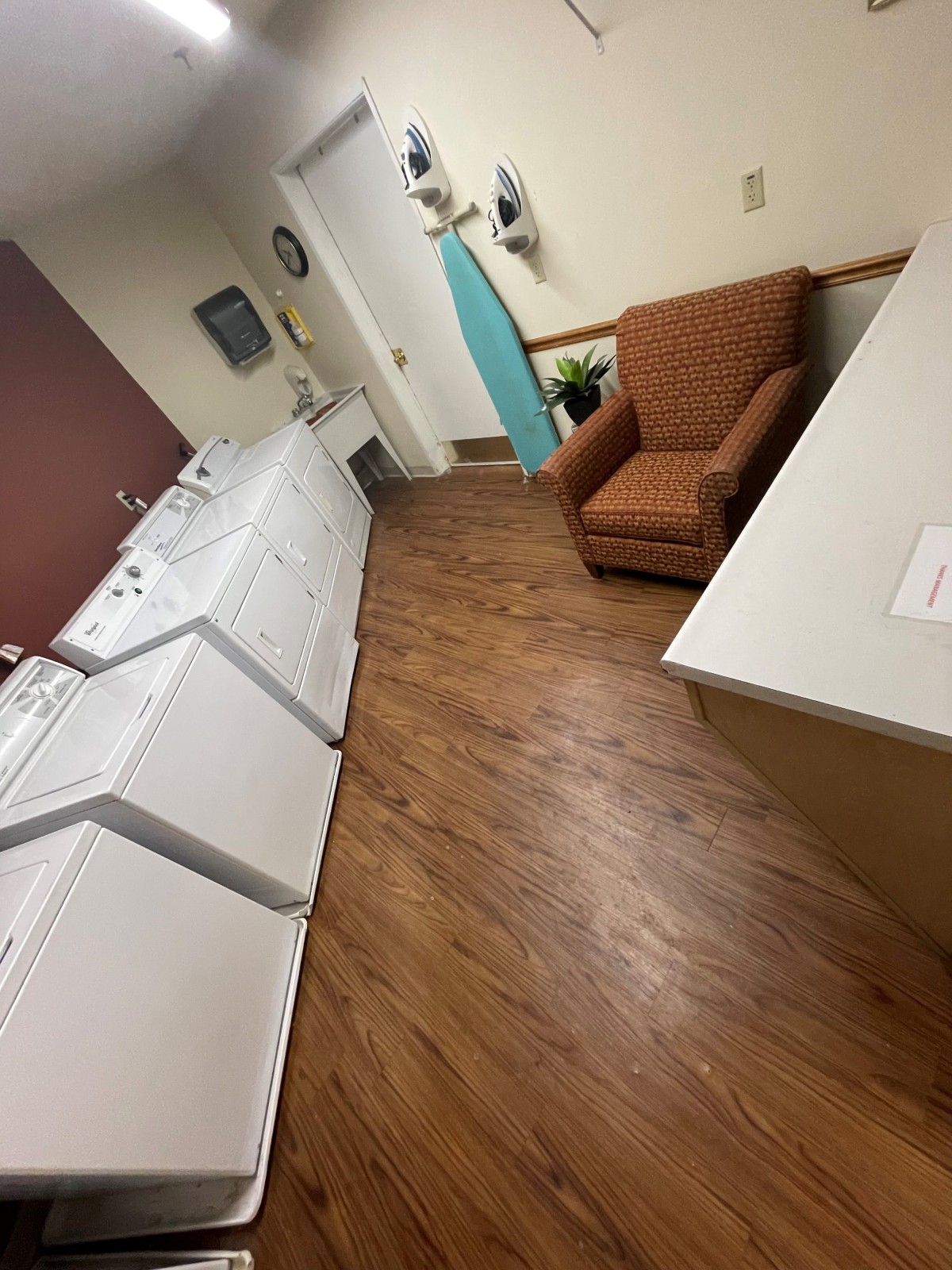 A cozy laundry room featuring washing machines, a dryer, an ironing board, and a comfortable chair.