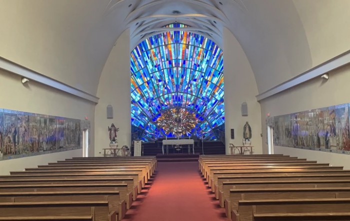 Interior view of a church featuring a vibrant stained glass window behind the altar.