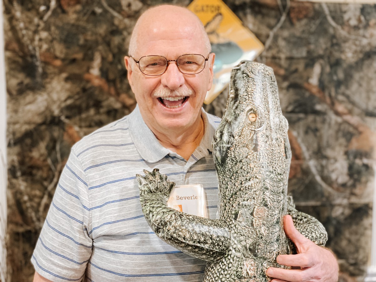 A man smiling while holding an alligator indoors.