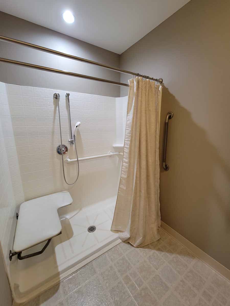 An accessible bathroom shower featuring a curtain, grab bars, and a foldable seat.