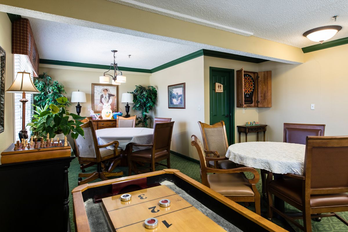 A cozy dining room with tables and chairs, decorated with plants and paintings.