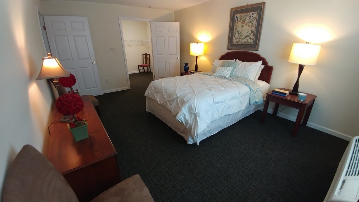 A cozy bedroom with a neatly made bed, nightstand, and lamp.