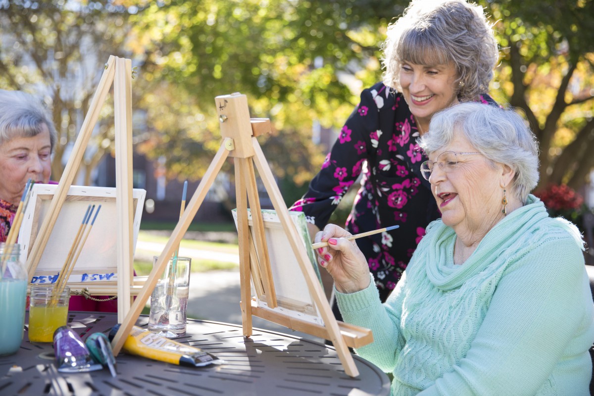 Elderly women enjoying a painting session outdoors on a sunny day.