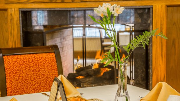 A cozy restaurant table setting with flowers and a fireplace in the background.