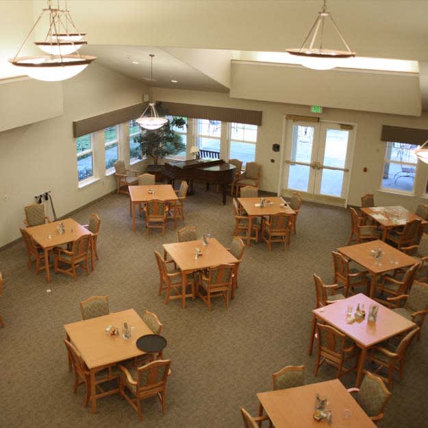 A spacious dining area with wooden tables and chairs, featuring large windows.