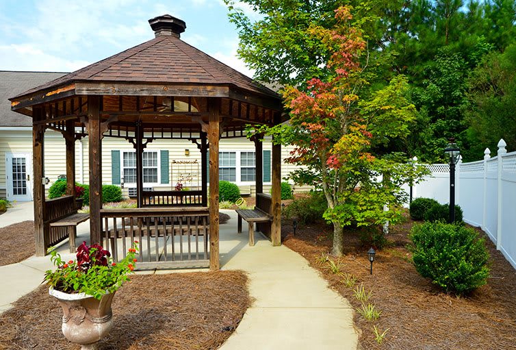 A wooden gazebo surrounded by a landscaped garden with a tree showing autumn colors.