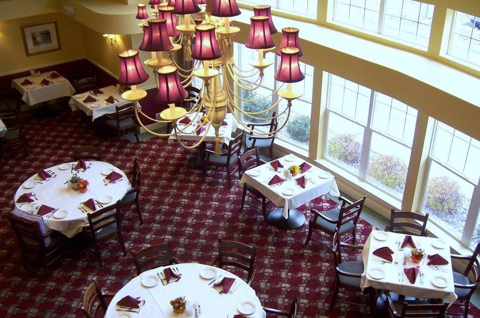 An elegant restaurant dining area with round tables, purple-accented chandeliers, and a carpeted floor.