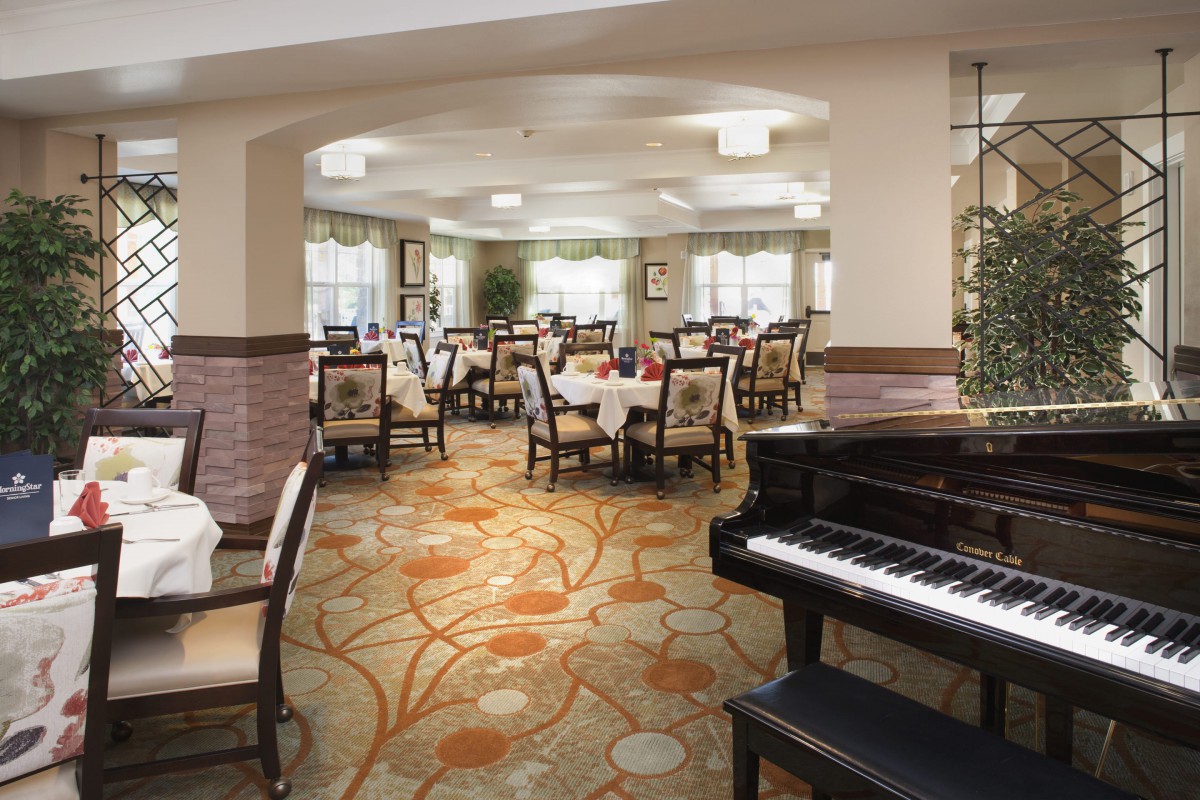 A well-decorated dining room with a grand piano and elegantly arranged tables.