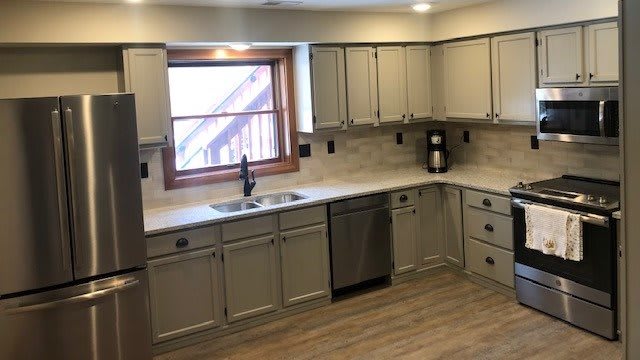 A modern kitchen with light-colored cabinets, a large window, and wood flooring.