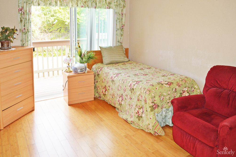 A cozy bedroom with a single bed featuring floral bedding, a side table, and natural light coming through a sliding door.
