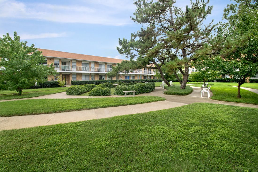A peaceful outdoor landscape with a pathway, trees, and a building in the background.