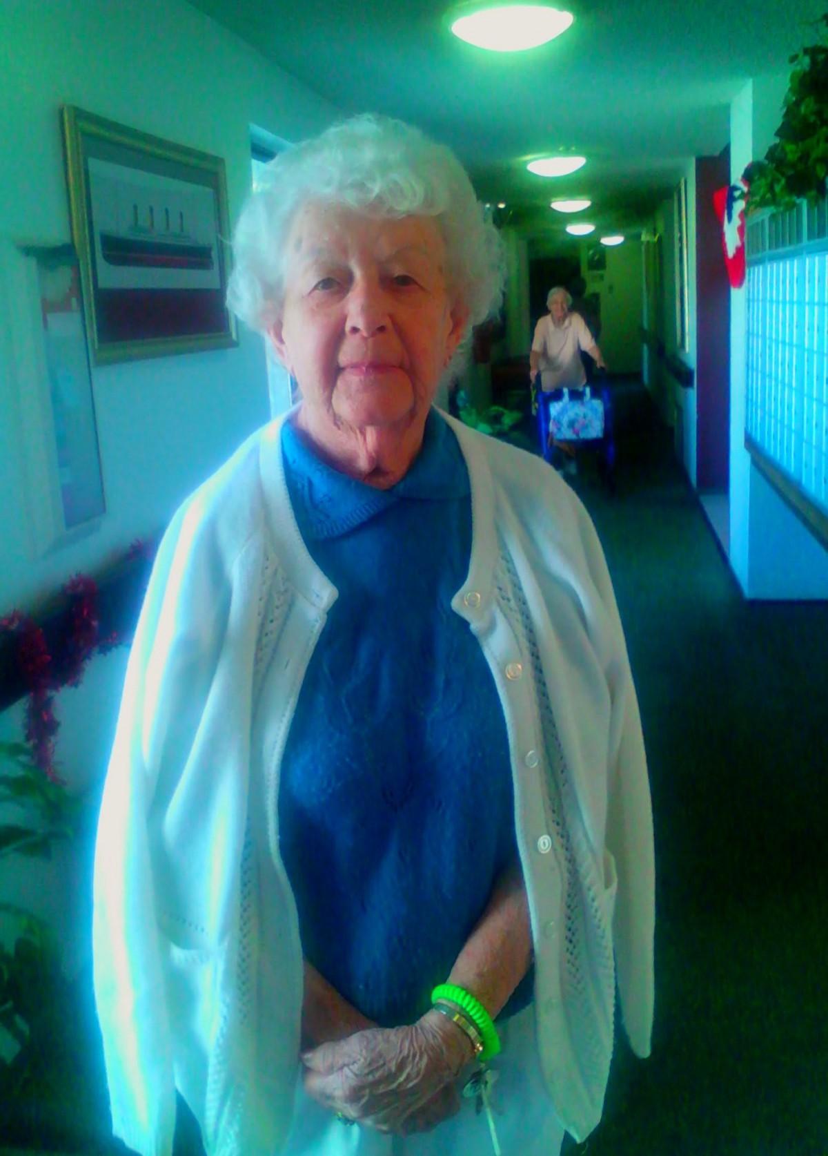 An elderly woman standing in a brightly lit hallway.