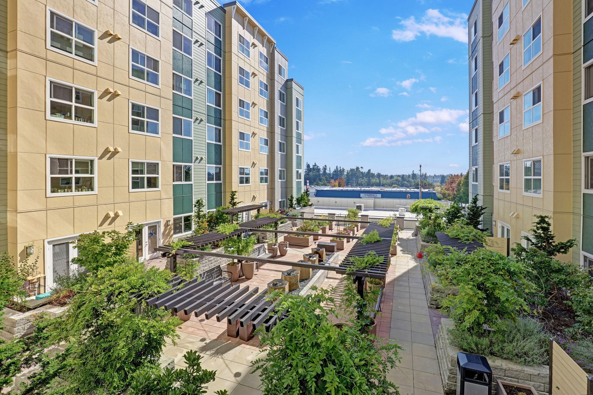 An outdoor courtyard area between apartment buildings featuring greenery and seating areas.