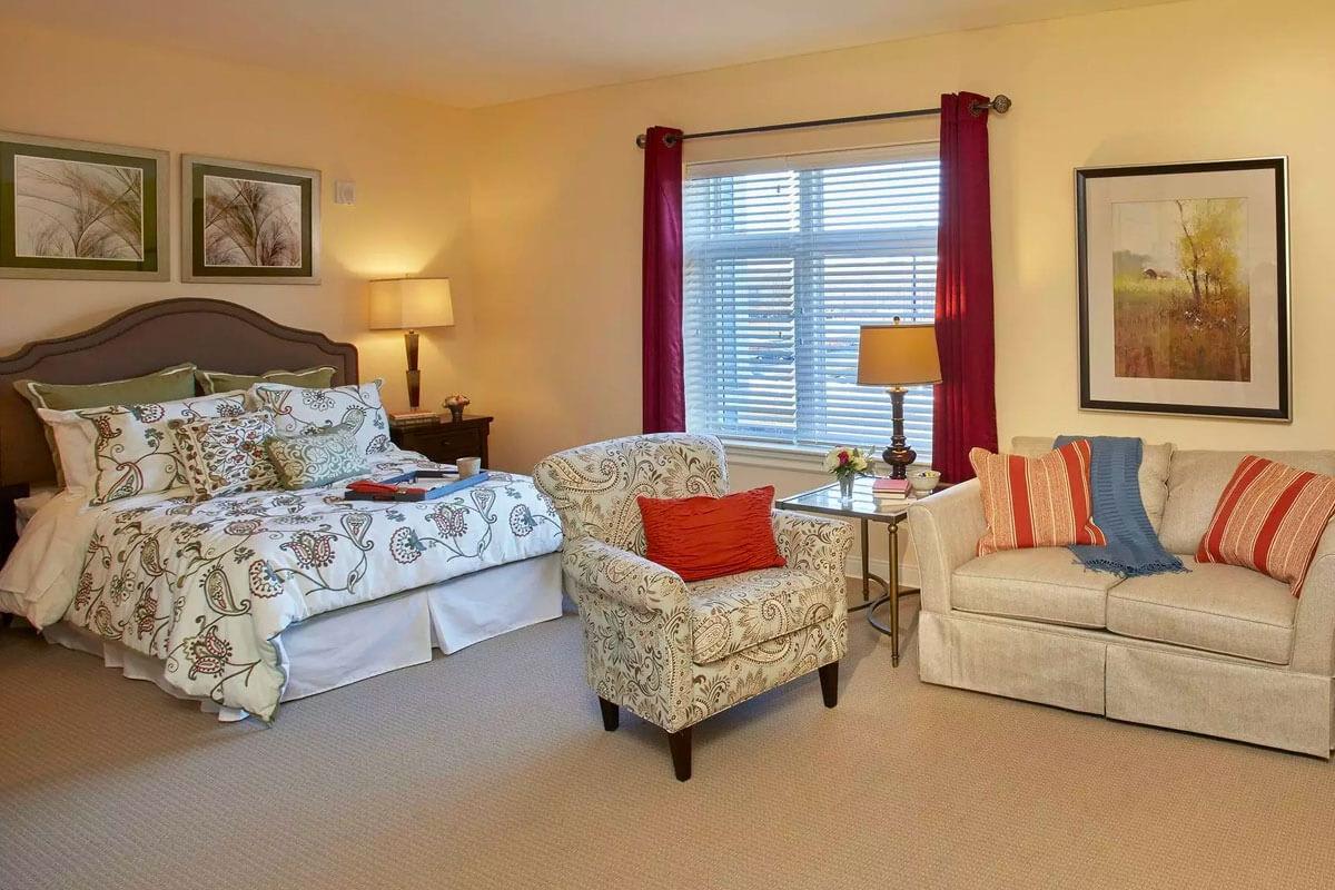 A cozy bedroom featuring a bed, armchair, and sofa with warm lighting and decorative pillows.