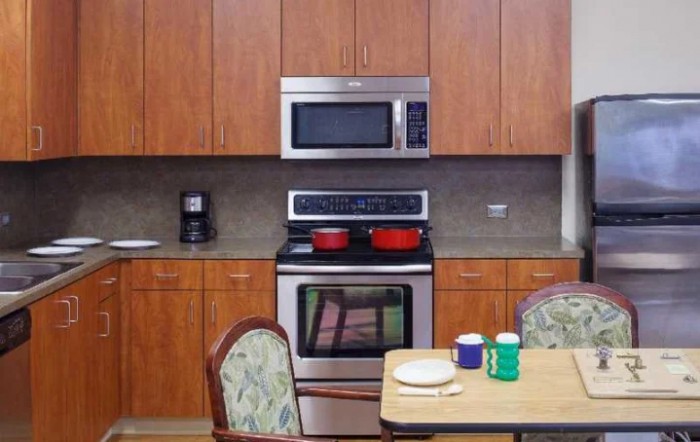 A kitchen with wooden cabinets, a stove, and a microwave, featuring a dining table set with cups.