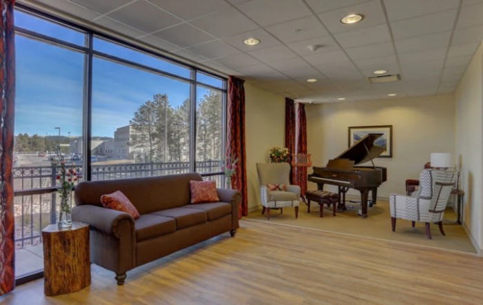 A cozy living room with a grand piano, comfortable seating, and large windows offering a scenic view.
