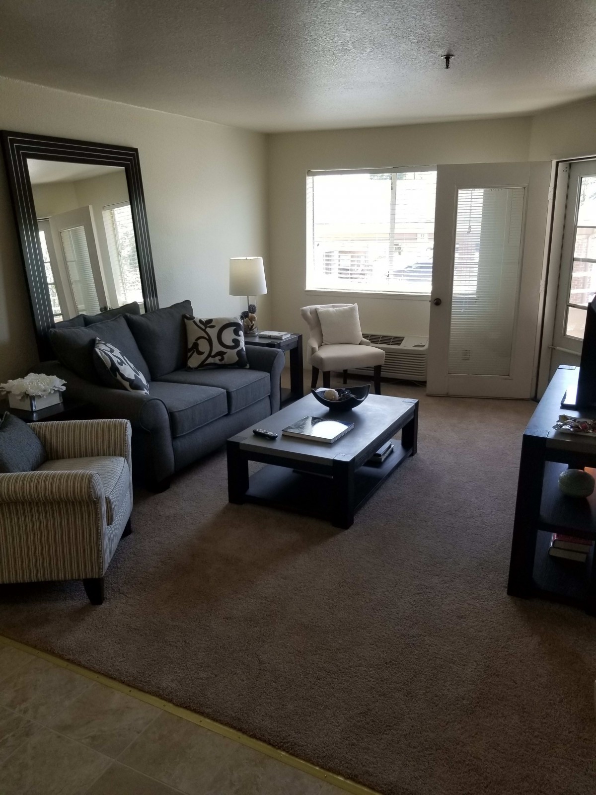 A cozy living room with a sofa, chairs, coffee table, and a large mirror.