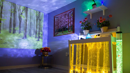 A cozy and vibrant room with ambient lighting, featuring a projector display of a forest scene, floral arrangements, and artistic decorations.