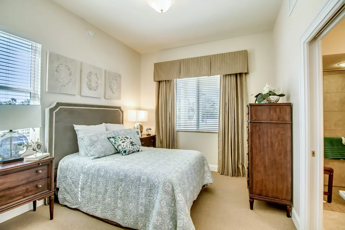 A cozy bedroom with a neatly made bed, an elegant dresser, and warm lighting.