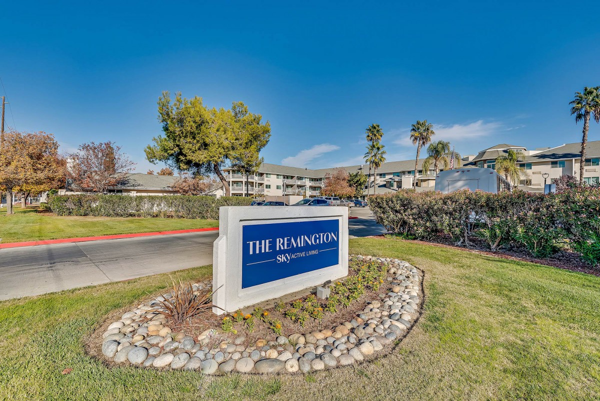 Outdoor sign for 'The Releighers' surrounded by greenery and trees, with buildings in the background under a clear blue sky.